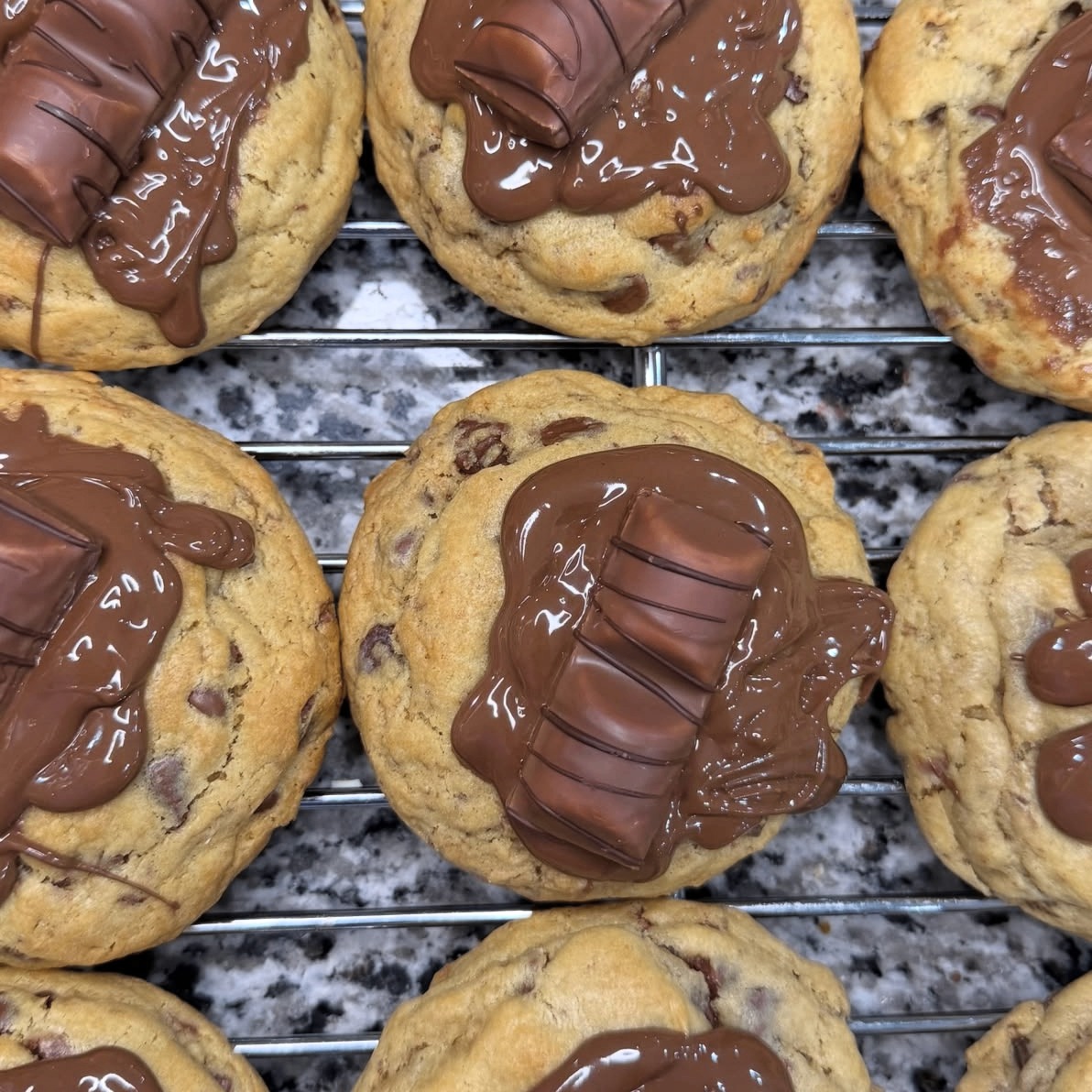 Chocolate chip cookies topped with melted Kinder chocolate bars, cooling on a rack